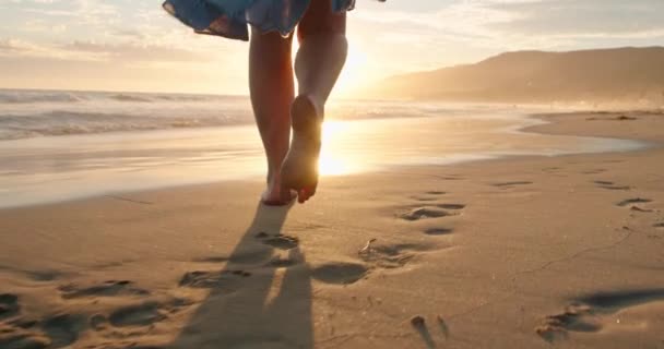 Крупним планом жінка ноги ходять босоніж на пляжі на золотому заході сонця залишаючи слід — стокове відео