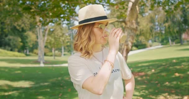 Giovane caucasica bella donna indossa elegante cappello bere caffè nel parco verde — Video Stock