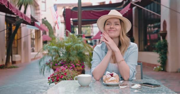Hermosa mujer está soñando despierto en el pequeño restaurante de la calle en el casco antiguo, 4K — Vídeo de stock