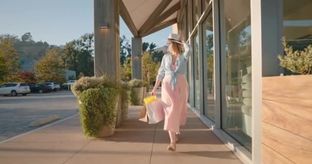 Attractive stylish woman in pink dress with paper bags walking by shopping mall — Stock Video