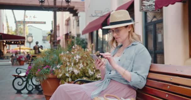 4K cámara lenta vacaciones en Europa. Mujer bonita está revisando el teléfono relajándose en el banco — Vídeo de stock