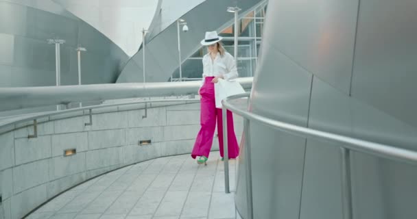 Mujer rubia bastante sonriente en aspecto elegante camina con confianza con bolsas de compras — Vídeos de Stock