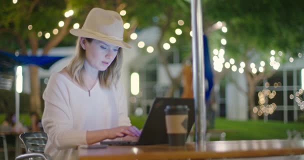 Business woman is typing on keyboard of her laptop on late summer night in park — Stock Video