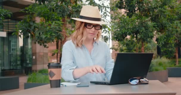 Kvinna frilansare arbetar på bärbar dator vid utomhus grön park i businesscenter — Stockvideo