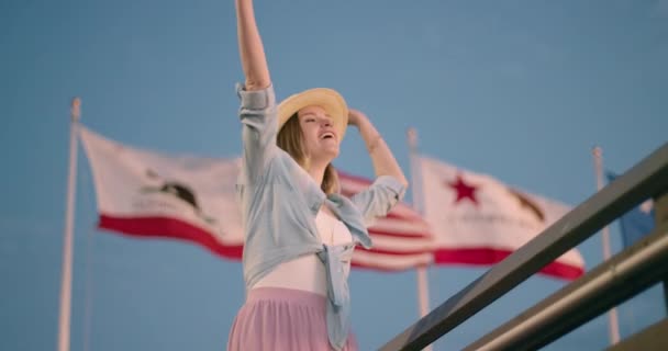 Mulher bonita feliz está dançando, Califórnia e bandeira americana acenando no fundo — Vídeo de Stock