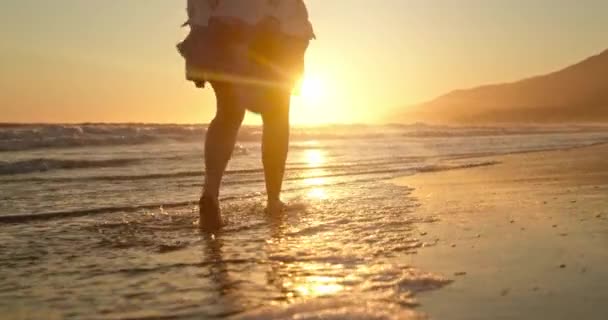 Femme au ralenti marchant pieds nus dans les vagues de l'océan dans la lumière dorée du coucher du soleil. 4K — Video