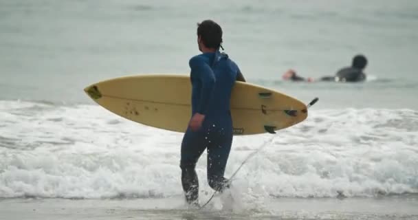 Пляж Малибу, Тихий океан 2020. Активный человек бежит в океан с доской для серфинга — стоковое видео