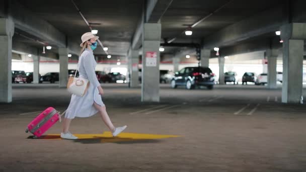 Femme masquée avec des bagages roses vient d'arriver à ses vacances. COVID-19 voyages — Video