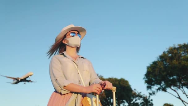 Wolno poruszająca się kobieta w masce na twarzy patrząc na zachód słońca, lądujący samolot na tle — Wideo stockowe
