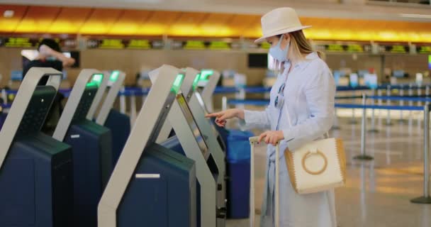 Mujer con máscara facial registrándose en la terminal vacía del aeropuerto. Viajes seguros COVID-19 — Vídeos de Stock