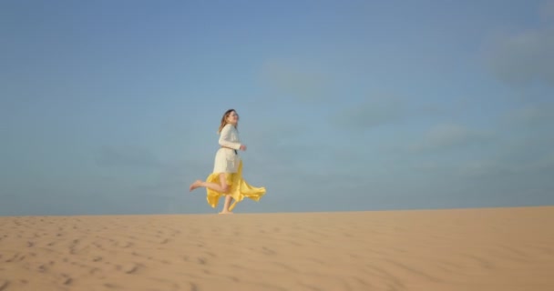 Медленное движение красивой женщины в льстивом платье, бегущей по волнистой песчаной дюне — стоковое видео