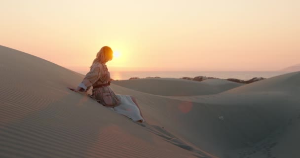 Кінематографічний знімок моделі моди, що сидить на піщаних дюнах, насолоджуючись прекрасною природою — стокове відео