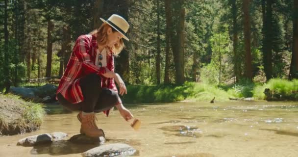 Lambat gerak wanita muda duduk di sungai hutan dan minum air jernih, 4K — Stok Video