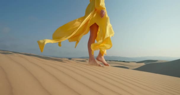 Dalgalı kum tepeciği yüzeyinde çıplak ayakla yürüyen moda elbiseli kızın yakın çekimi, 4K — Stok video