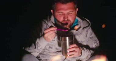 Yakışıklı adam hafta sonları kamp yapmaktan hoşlanıyor. Adam yemek yiyor ve kamp ateşine bakıyor, 4K