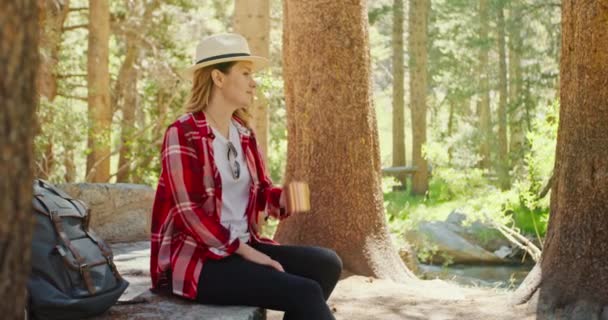 Ralenti femme souriante assoiffée de mouvement assis dans la forêt verte et l'eau potable, 4K — Video