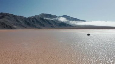 Ölüm Vadisi Çölü 'nün ıslak çatlak yüzeyinde kara kayaların etrafında uçan drone.