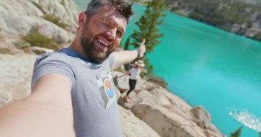 Gölde mutlu romantik bir çift. Neşeli adam manzaralı mavi göl 4K 'de selfie çekiyor.