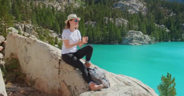 Slow motion happy traveler woman sitting on the rock with scenic blue lake view — Stock Video
