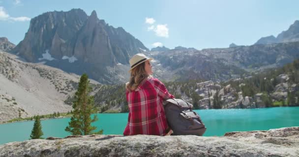 Mujer disfrutando de la vista de la naturaleza cinematográfica. Viajero de vista trasera sentado en el lago azul 4K — Vídeo de stock