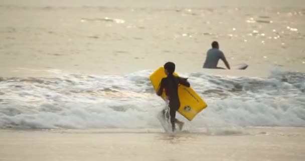 4K chico en cámara lenta en el surf con boogie board amarillo corriendo en el océano — Vídeo de stock