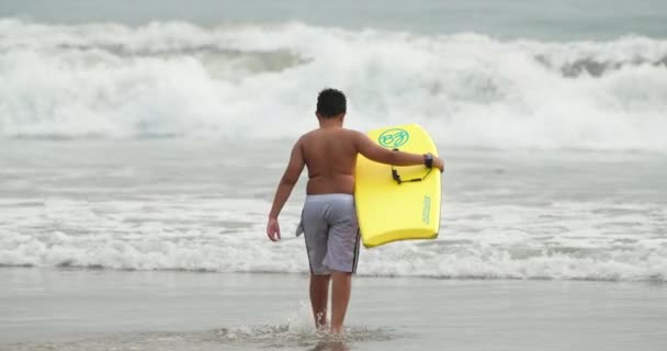 Slow motion 4K tonåring pojke surfa med gul boogie styrelse promenader i havet — Stockvideo