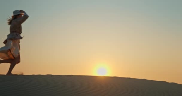 Щаслива збуджена жінка біжить піщаною дюною з золотим заходом сонця на фоні, 4K — стокове відео