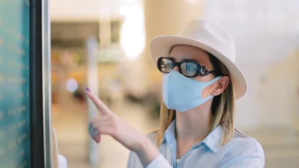 Reisende mit blauer Gesichtsmaske checken Flüge auf Stundenplan-Bildschirm auf leerem Flughafen — Stockvideo