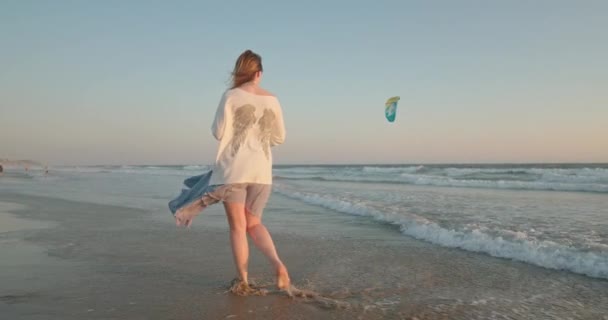 Kvinna njuter av solnedgången på stranden 4K. Modell som tittar på drake flyger över havet — Stockvideo