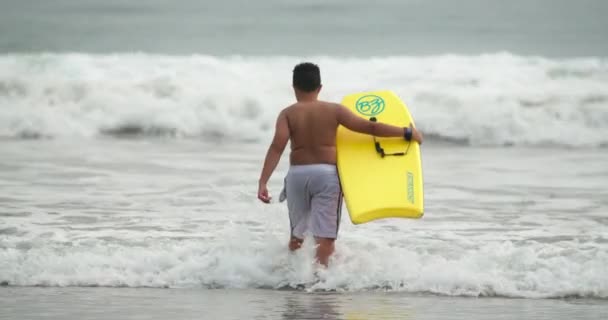 Rallentatore 4K adolescente ragazzo surf con giallo boogie bordo a piedi in oceano — Video Stock