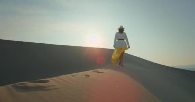 Dalgalı doku yüzeyine sahip, kumlu kumların yanından geçen bir kadının arka görüntüsü. 4K