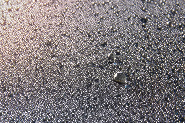 Water droplets on the glass glisten in a beam of light on a black background, close-up texture