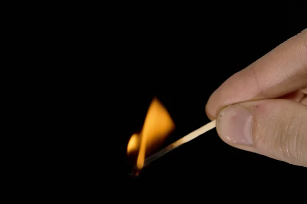 burning match in hand on black background