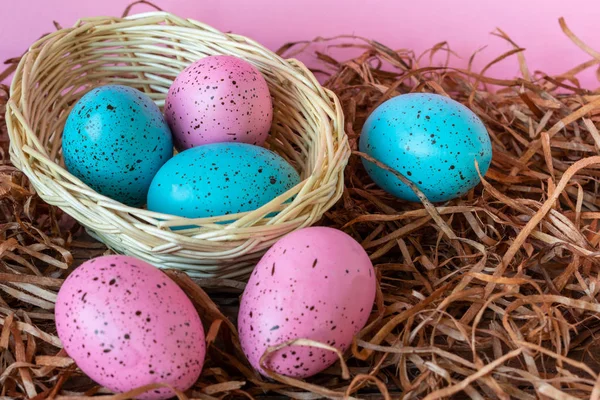 Six pink and blue Easter eggs in a basket on pink and straw  background. Close-up Easter celebratory wallpaper.