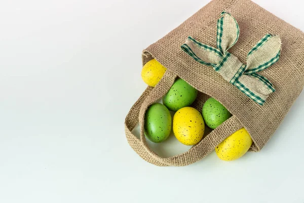 Yeşil ve sarı benekli yumurtalar bir rustik jüt poşet beyaz izole arka planda. Kopya alanı ile kutlama Paskalya duvar kağıdı.