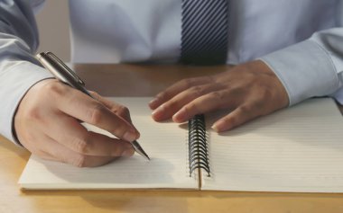 Masanın üzerine bir not kitabı yazan bir adamın yakın çekim görüntüsü.