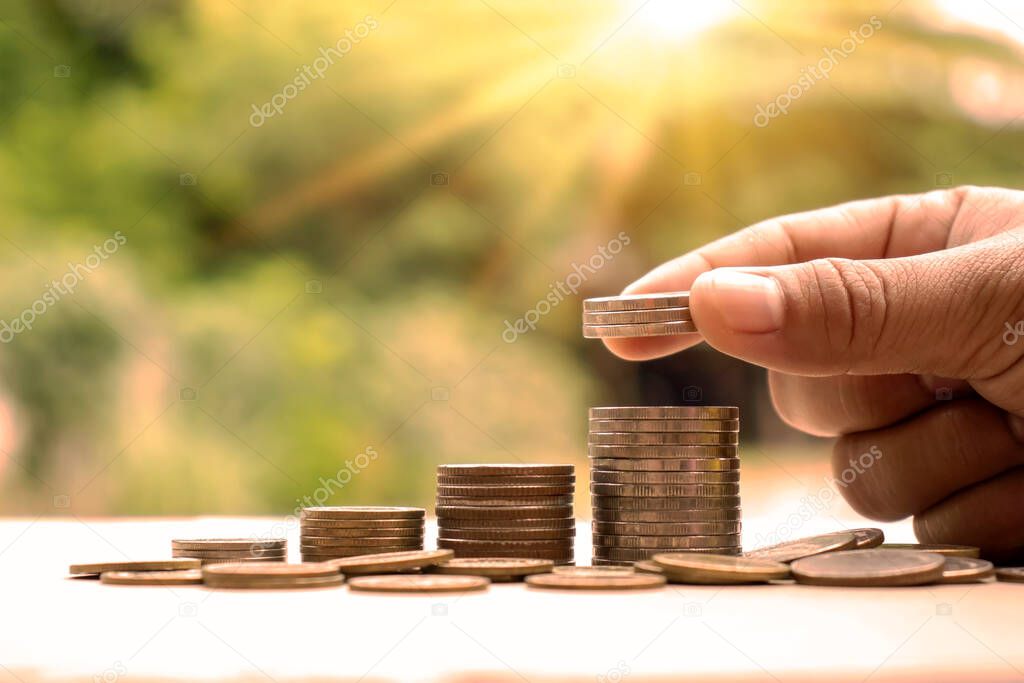 The man's hand placed a coin on a pile of coins that increased with the idea of economic growth and money saving.