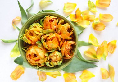 Bir yuvarlak kase, yeşil yaprakları ve sarı güzel turuncu laleler