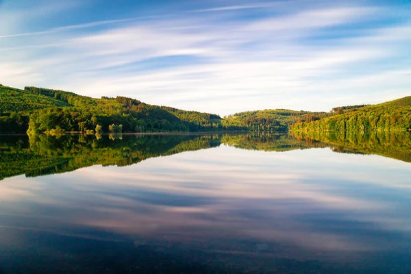 Long exposure of the Hennesee near Meschede in the early morning hours. Symmetrical image with trees mirrored in the water. Sauerland, Hochsauerland, Germany, wallpaper, background.