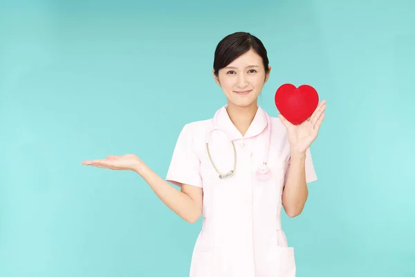 Smiling Asian nurse holding red heart love symbol