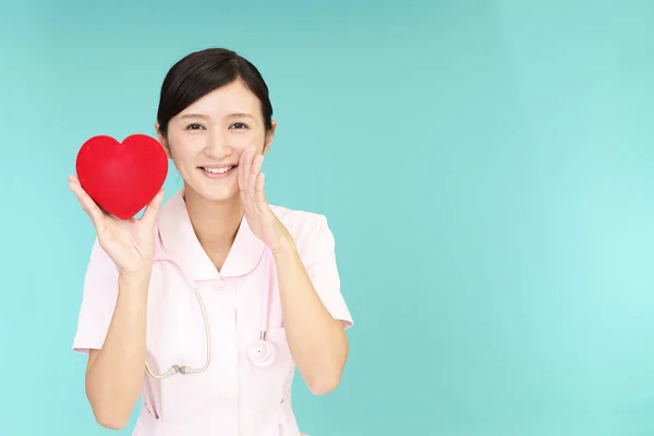 赤いハートの愛のシンボルを保持している笑みを浮かべてアジアの看護師 — ストック写真