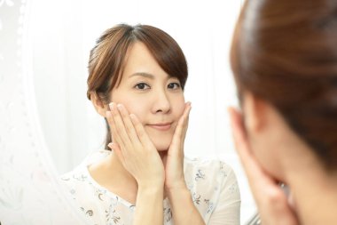 Asyalı kadın aynada yüzüne bakıyor.