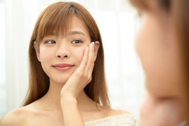 Asyalı kadın aynada yüzüne bakıyor.