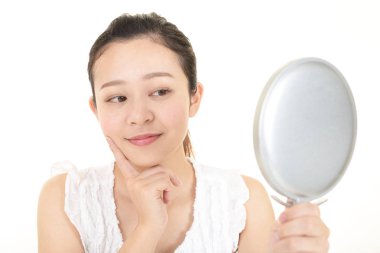 Asyalı kadın aynada yüzüne bakıyor.