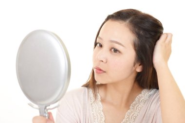 Asyalı kadın el aynasında saçlarına bakıyor