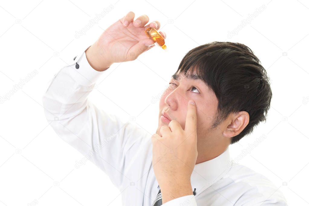 Asian businessman dripping eye with eyes drops.