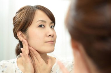 Asyalı kadın aynada yüzüne bakıyor.