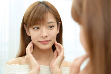 Asyalı kadın aynada yüzüne bakıyor.