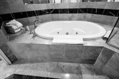 Beyaz jakuzi küveti ve mermer fayanslarla süslenmiş pirinç musluklar.