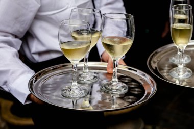 Garson elinde beyaz şarap kadehiyle bir tepsi tutuyor. Yüzü görünmüyor. beyaz üniforma.